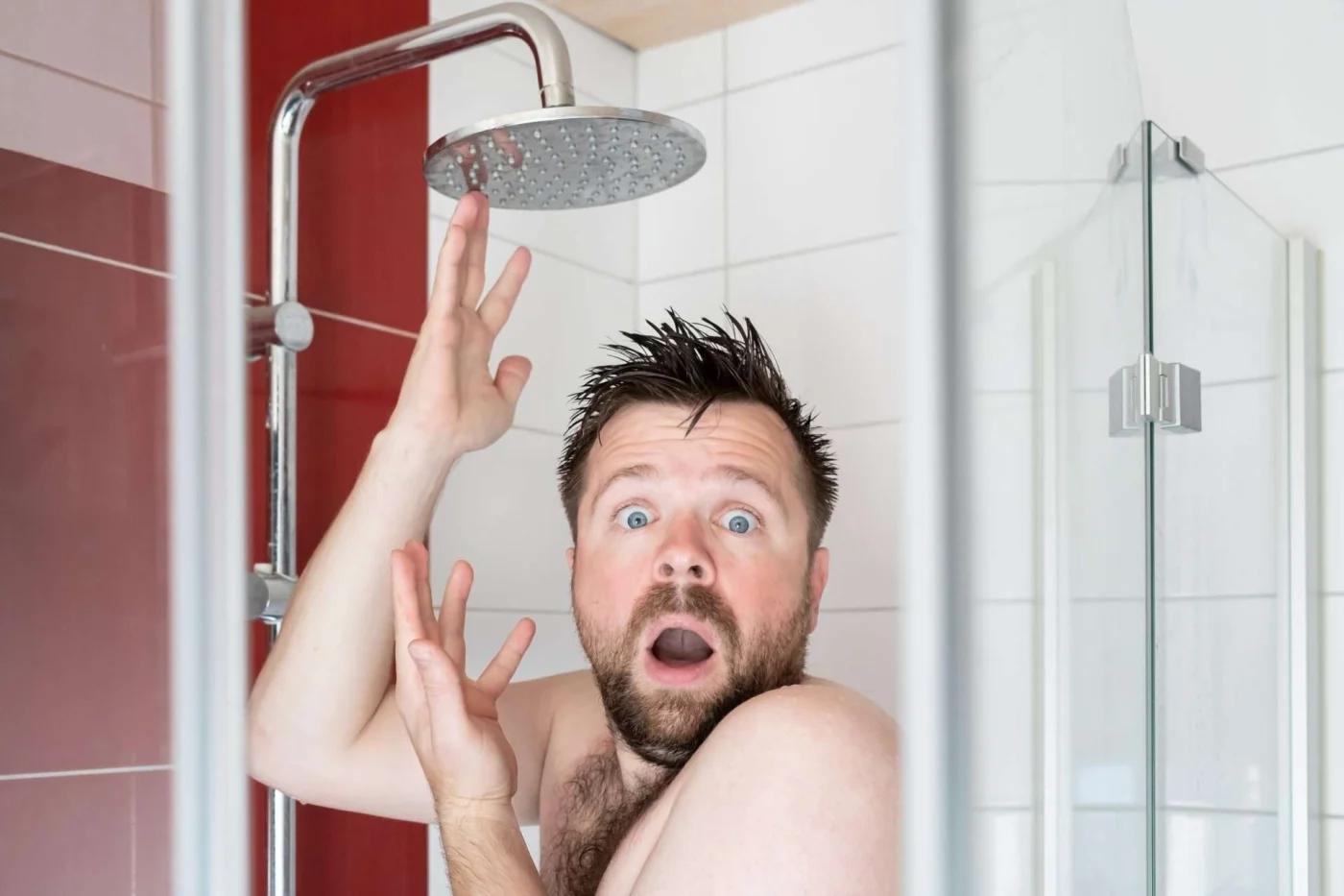 Frustrated man in dry shower, symbolizing a bathroom remodel mistake like poor plumbing planning