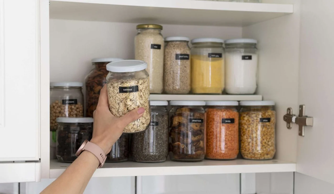 Close-up of hand organizing jars in cabinet, representing practical kitchen storage solutions during a remodel