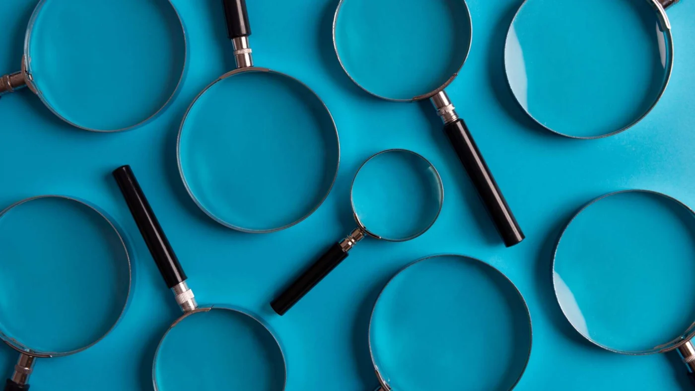 A series of evenly-spaced traditional-looking magnifying glasses of various sizes lying on a dark blue surface and pointed in different directions