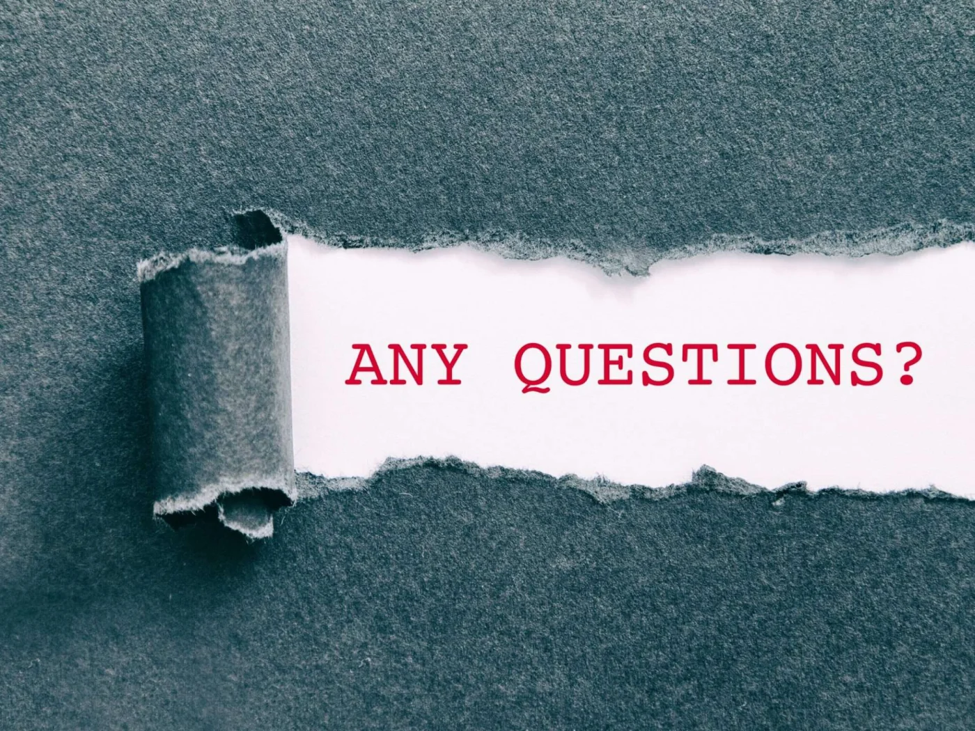 A closeup of a manilla folder with a tiny tear in it revealing the words, “any questions?”