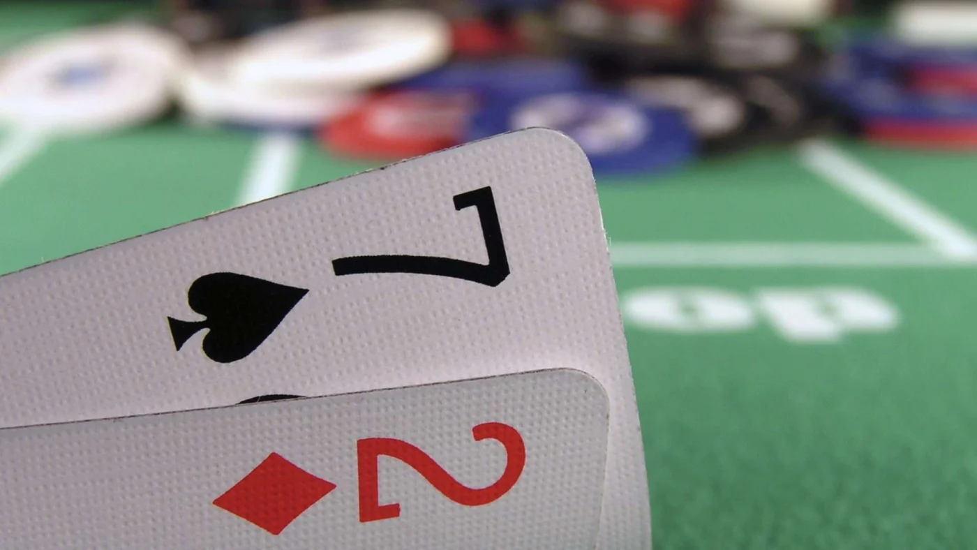 Close up of a 7 of spades and a 2 of diamonds with pokers chips in background