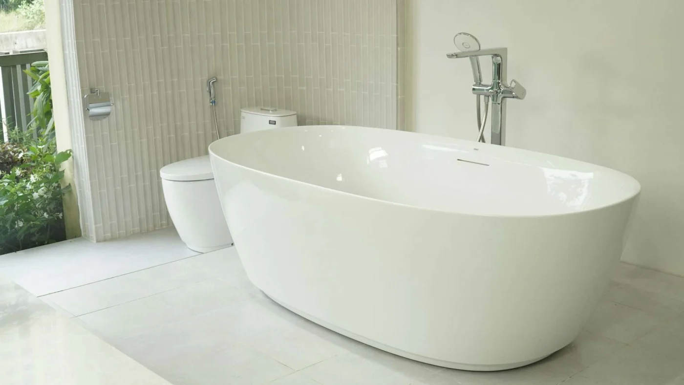 white flat bathtub with an attached shower head and white toilet next to it. White floors and white walls