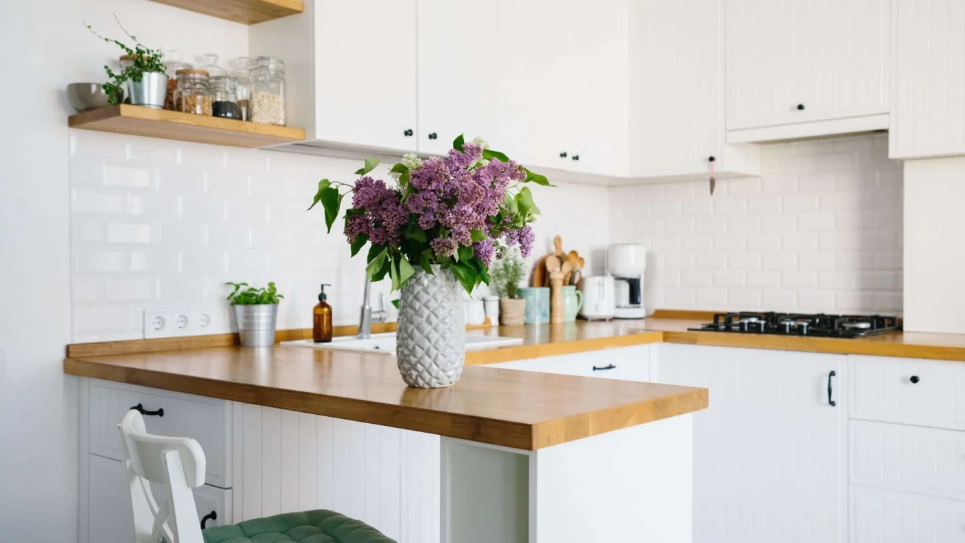 Kitchen with white cabinets, wood countertops, and a vase of purple flowers on the counter