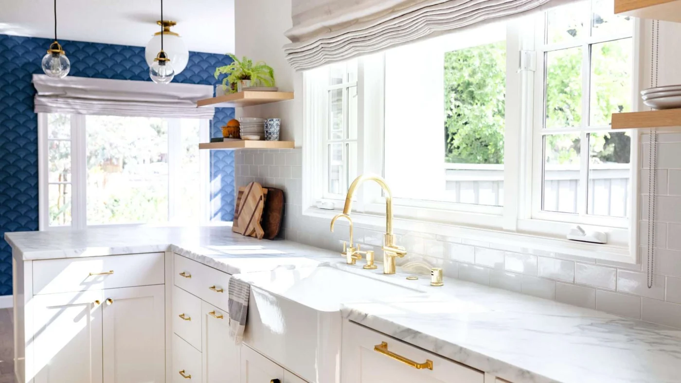 A stunning kitchen with marble countertops, gold fixtures, a blue accent wall, and natural light