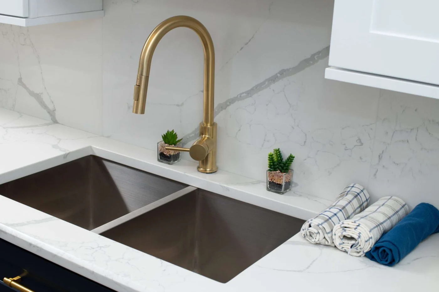 A sink with a brass faucet in a home with white and gray countertops