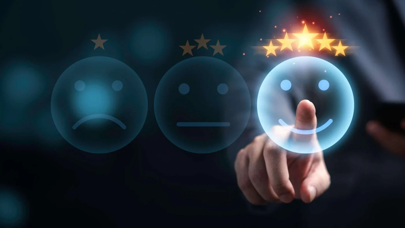 Three face icons are on a screen with the leftmost frowning with one star, the middle a neutral face with three stars, and the right smiling with five stars and being selected by a finger