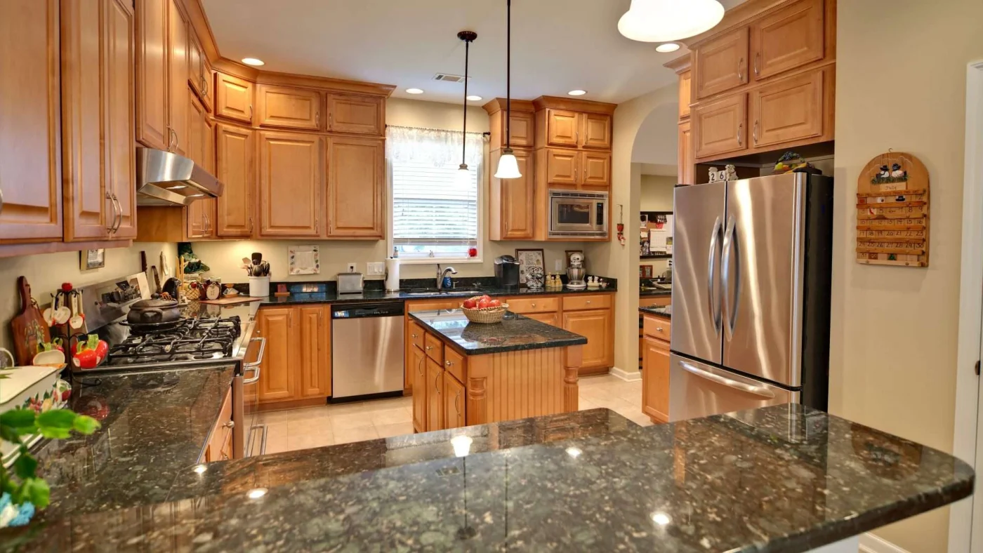 Newly remodeled Kansas City, MO kitchen with dark stone countertops, wooden cabinetry, and bright tile flooring