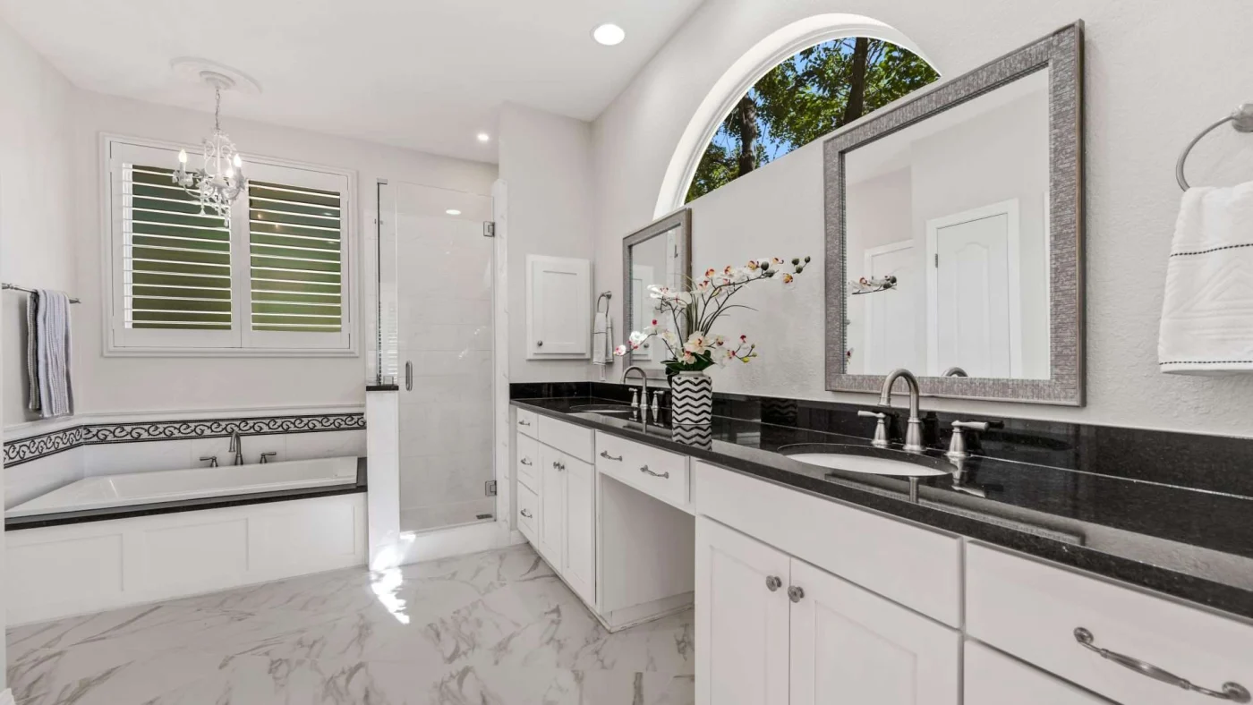 A large bathroom with white cabinets, black countertops, a double vanity, a bathtub, and a walk-in shower