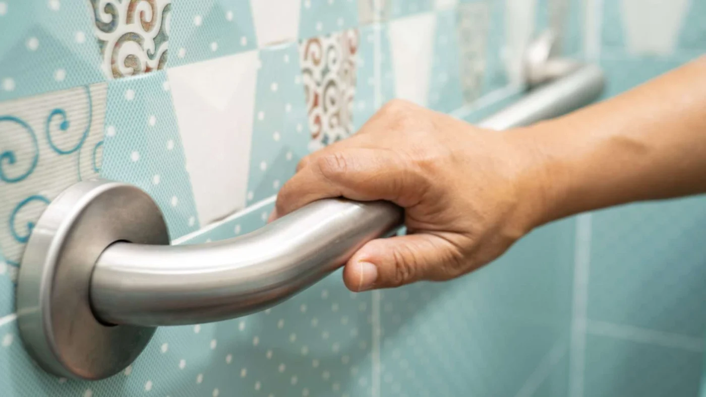 A person uses a grab bar in a bathroom