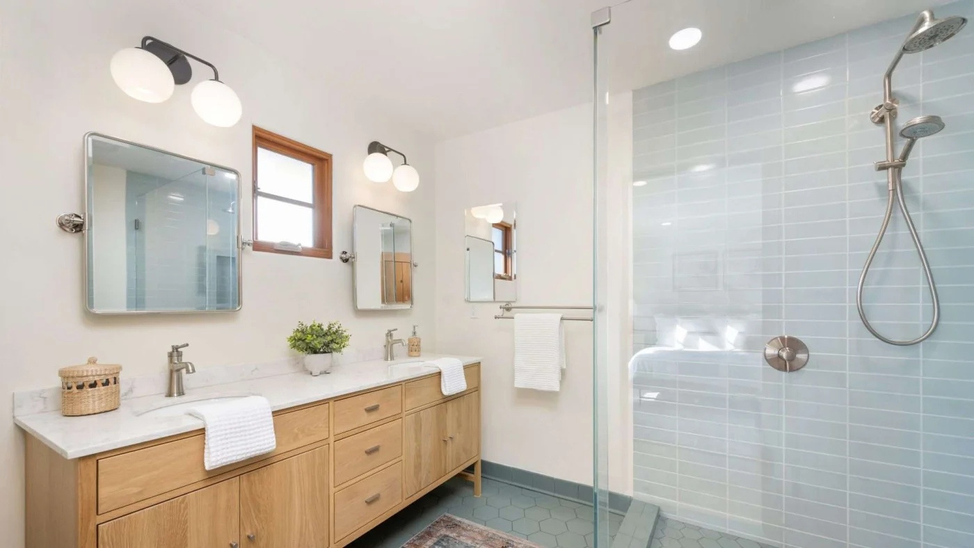 A bathroom with a light brown vanity, white countertops, and a walk-in shower with silver fixtures