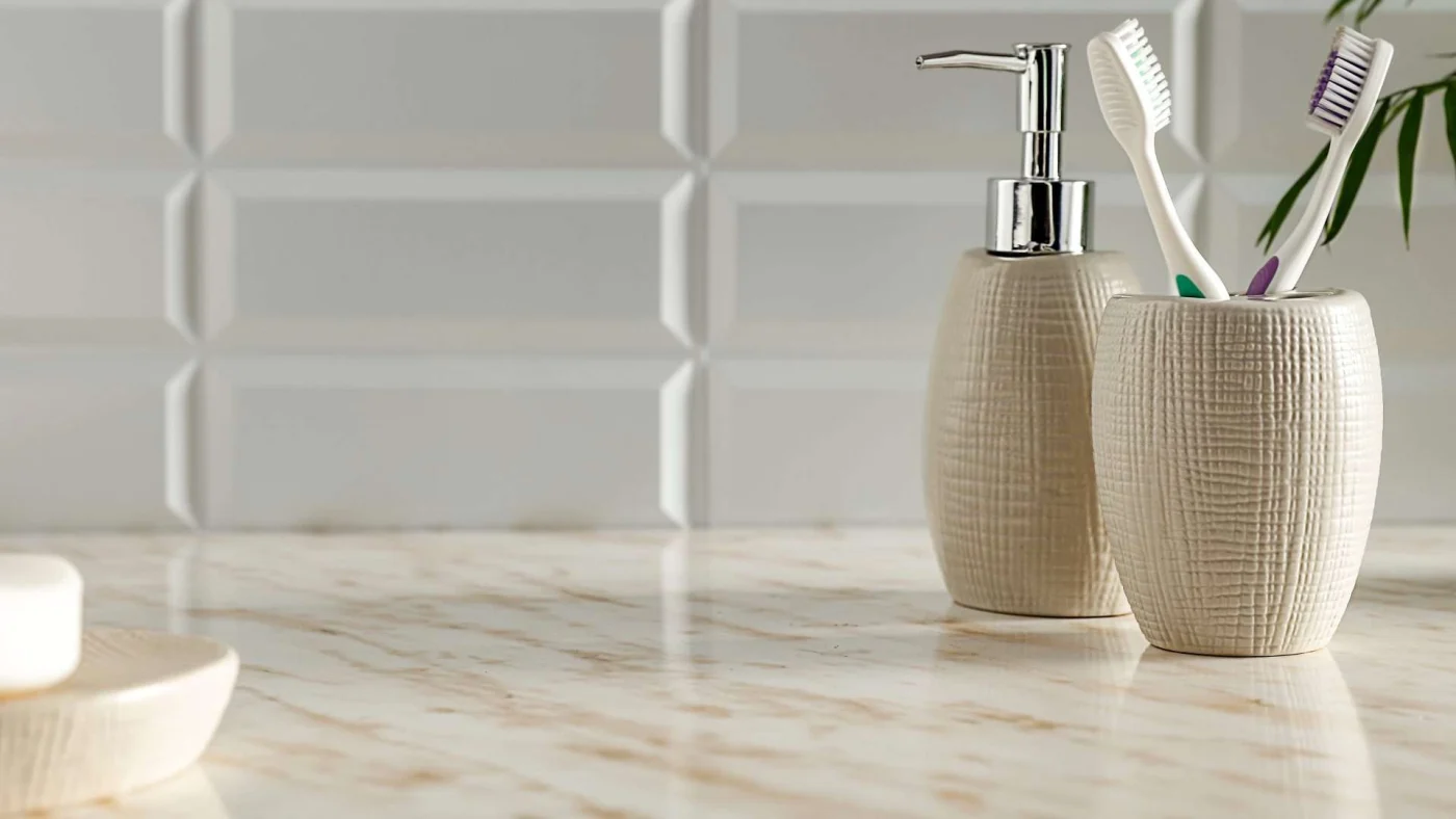 Closeup of a marble bathroom countertop with a toothbrush holder, soap dispenser, and bar of soap