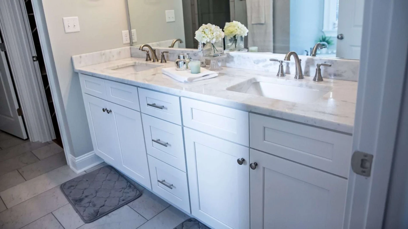 A bathroom vanity with white cabinets, a gray countertop, and double basin