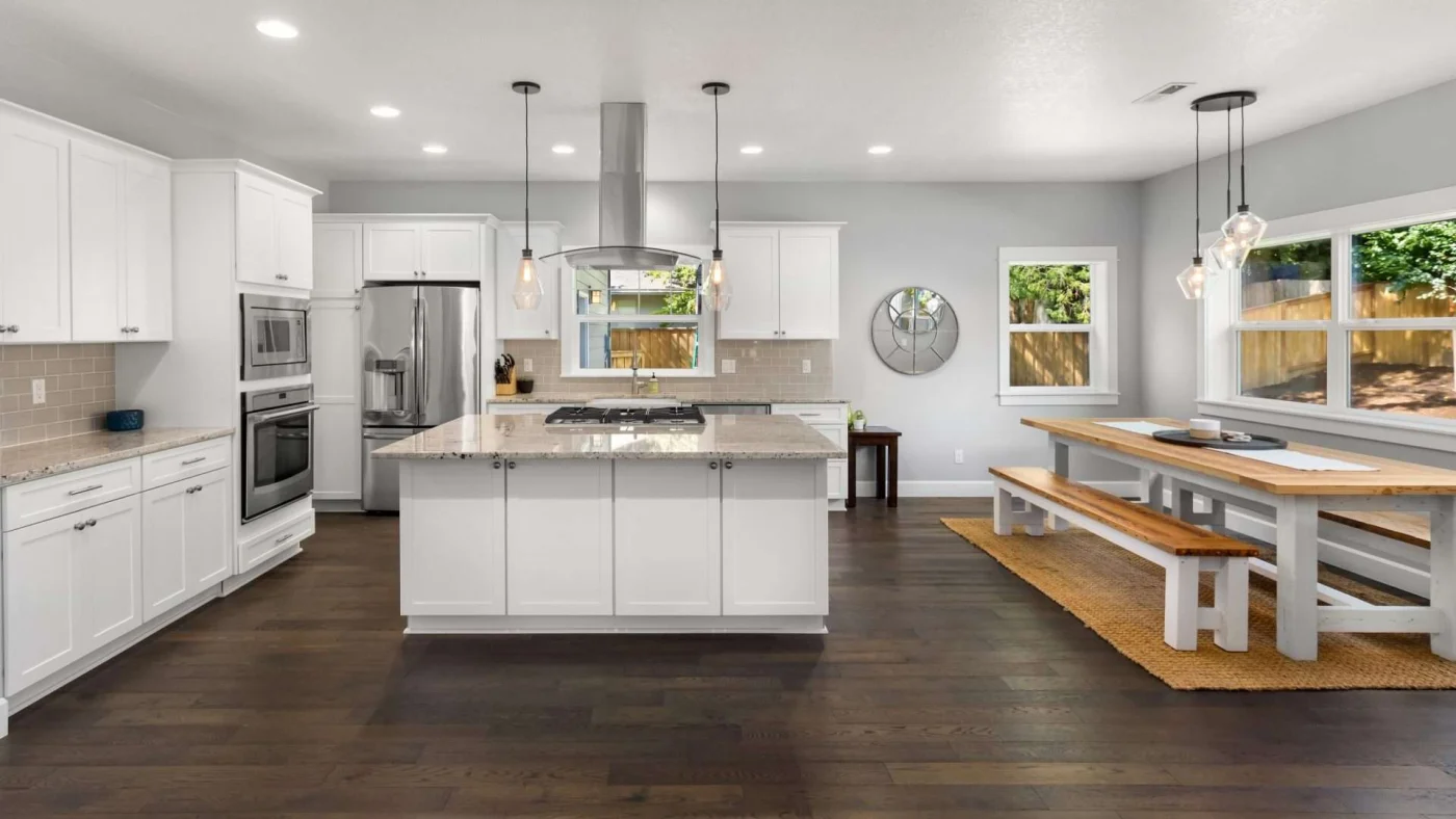 Open-concept kitchen with dark wooden flooring and bright white cabinets and wooden dining table