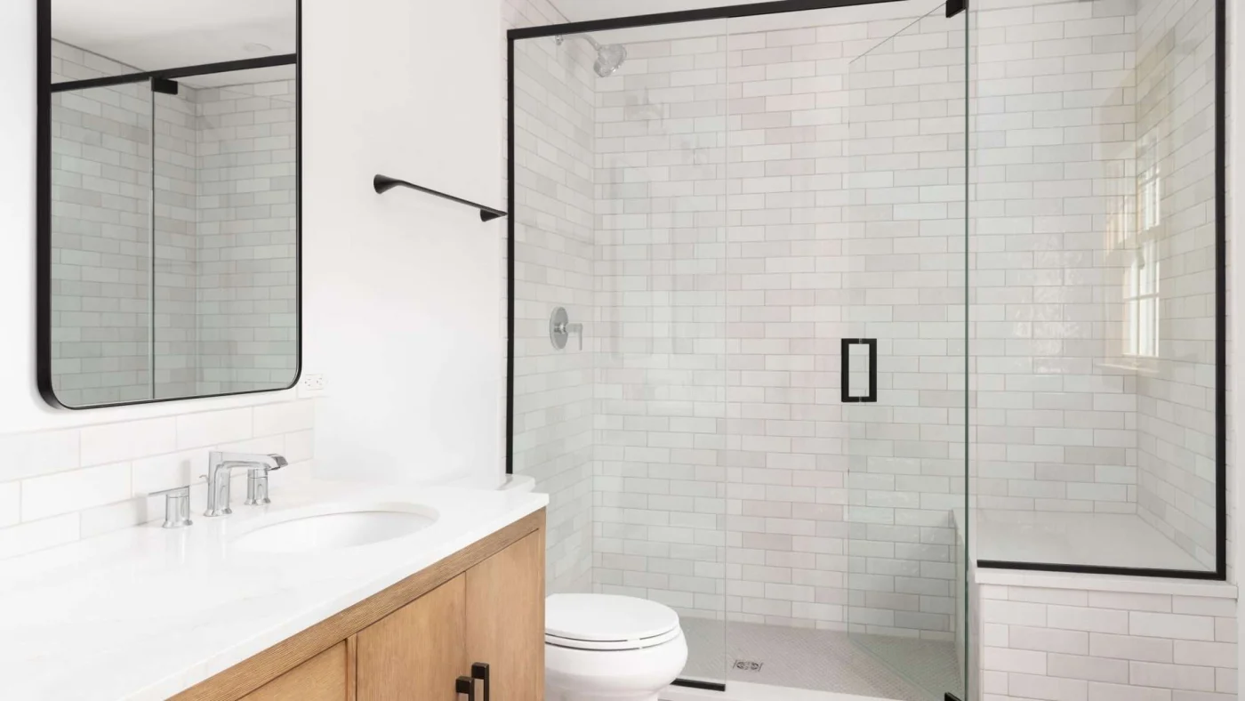 Newly remodeled bathroom with beautiful tile shower with glass doors and white sink countertop