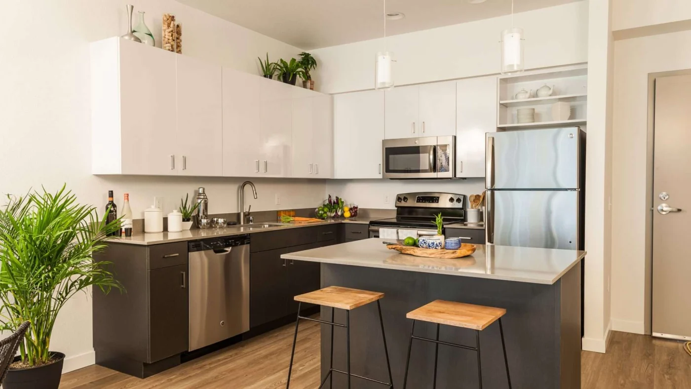 A kitchen with black cabinets on the bottom and white cabinets on top with silver appliances and finishes
