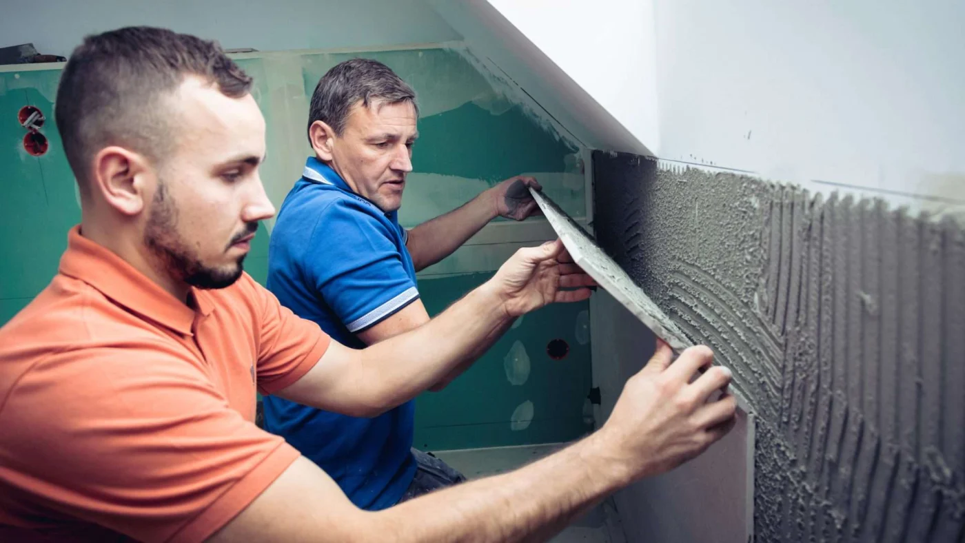 Close view of two installers carefully putting a large piece of bathroom tile into place