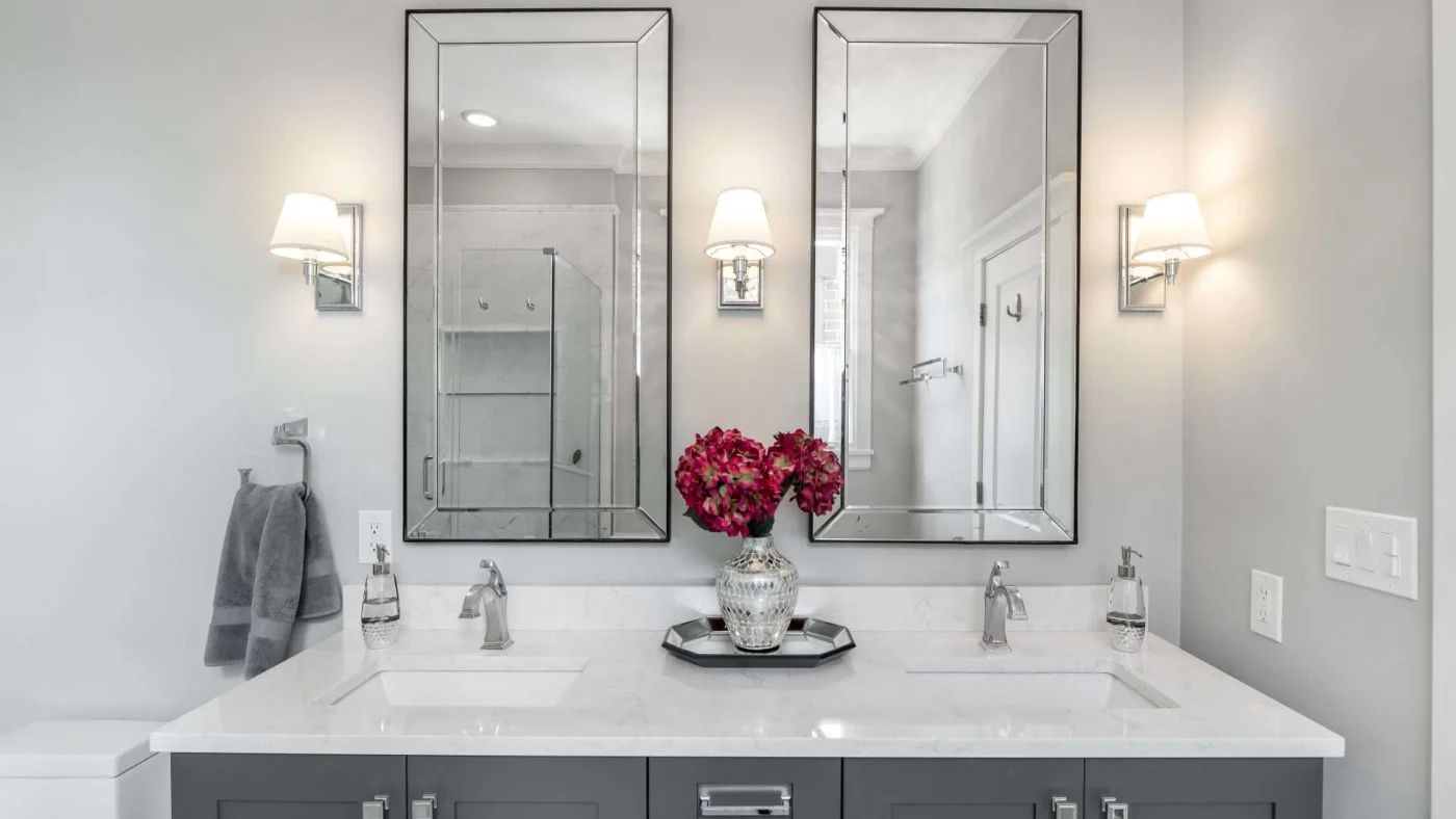 Newly remodeled bathroom with dual vanity mirror and sinks with white countertop and dark gray cabinetry