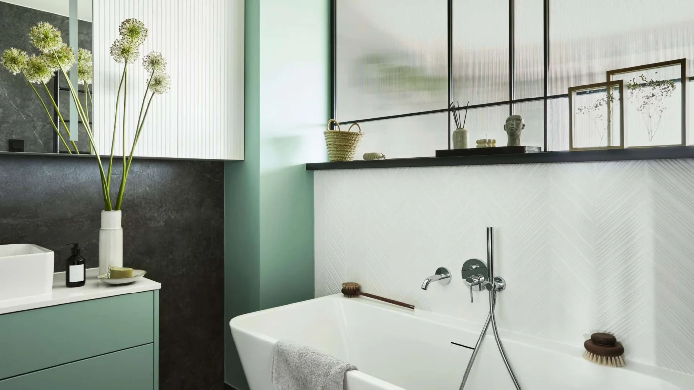 Close, angled view of a modern remodeled bathroom with a bathtub, vessel sink, and a half-wall topped with a glass panel