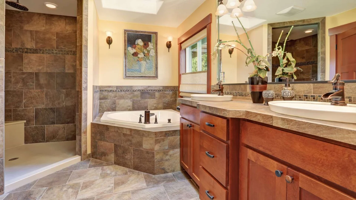 Newly remodeled bathroom with large brown tile walls and flooring and wooden cabinetry