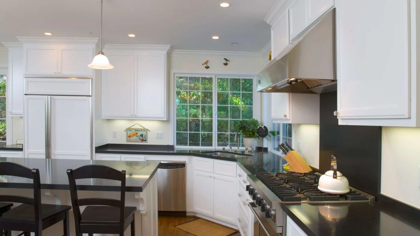 A kitchen with white cabinets, black countertops, an island, and stainless steel appliances