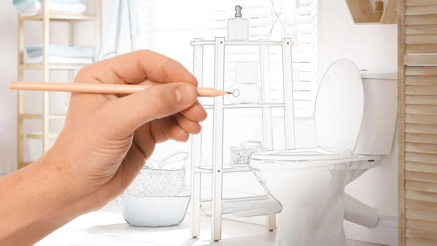 A hand sketches the finishing touches on a bathroom remodeling plan