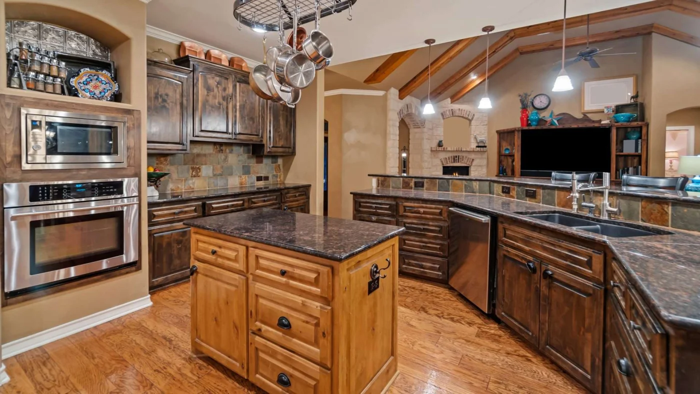 Beautiful kitchen remodel with dark wooden cabinets, hardwood flooring, hanging lights, and large dark stone cabinets