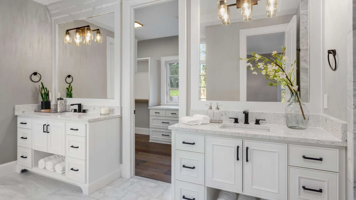 Close view of matching vanities in a new bathroom flanking an open door leading to a huge closet
