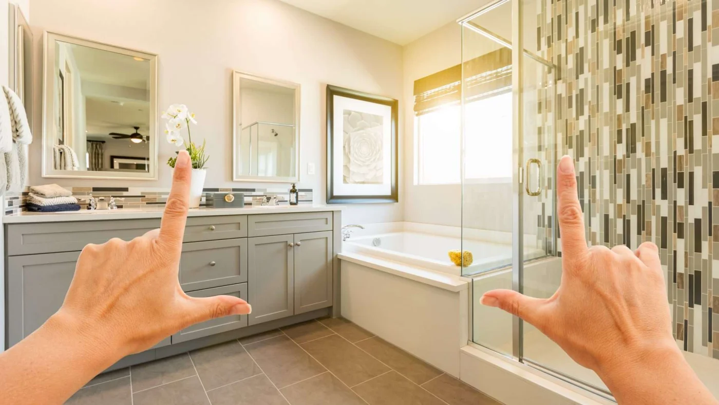 Two hands held up in front of a luxury bathroom with gray cabinets, a bathtub, and walk-in shower