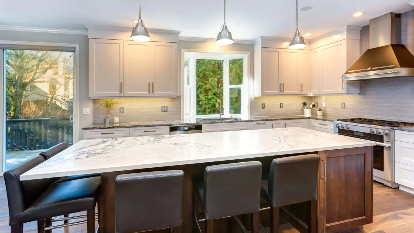 Modern home kitchen with white cabinets, marble countertops, and beautiful large window and sliding glass door