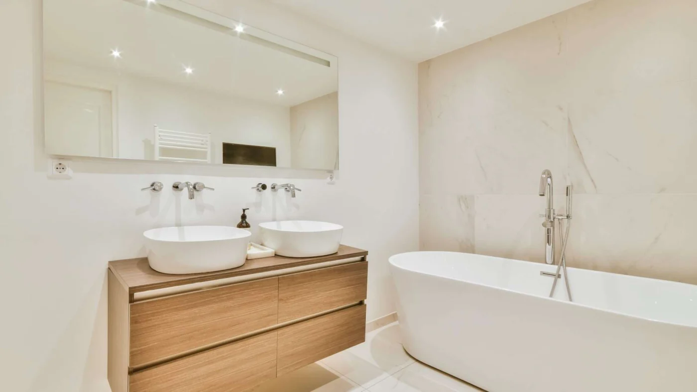 Close view of a sleek modern bathroom with a large, freestanding tub and a wood vanity topped with bowl sinks