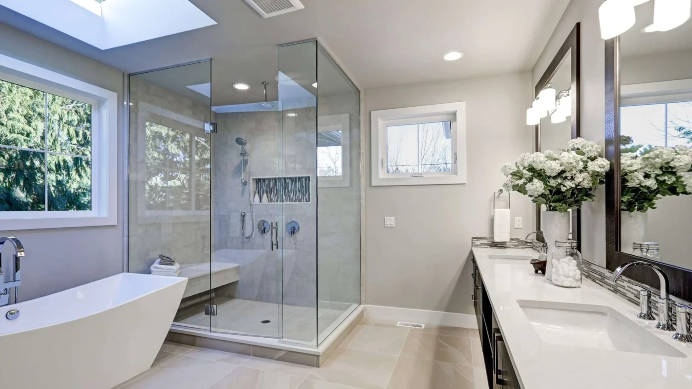 Long view of a large contemporary bathroom with a vanity on one wall, a bathtub on the other underneath a skylight, and a separate shower stall