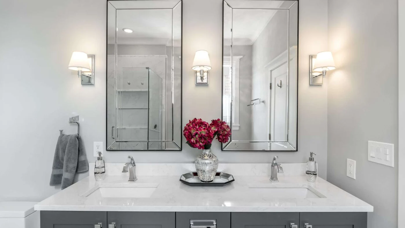 Frontal view of a beautiful gray vanity with double sinks and matching mirrors and sconces
