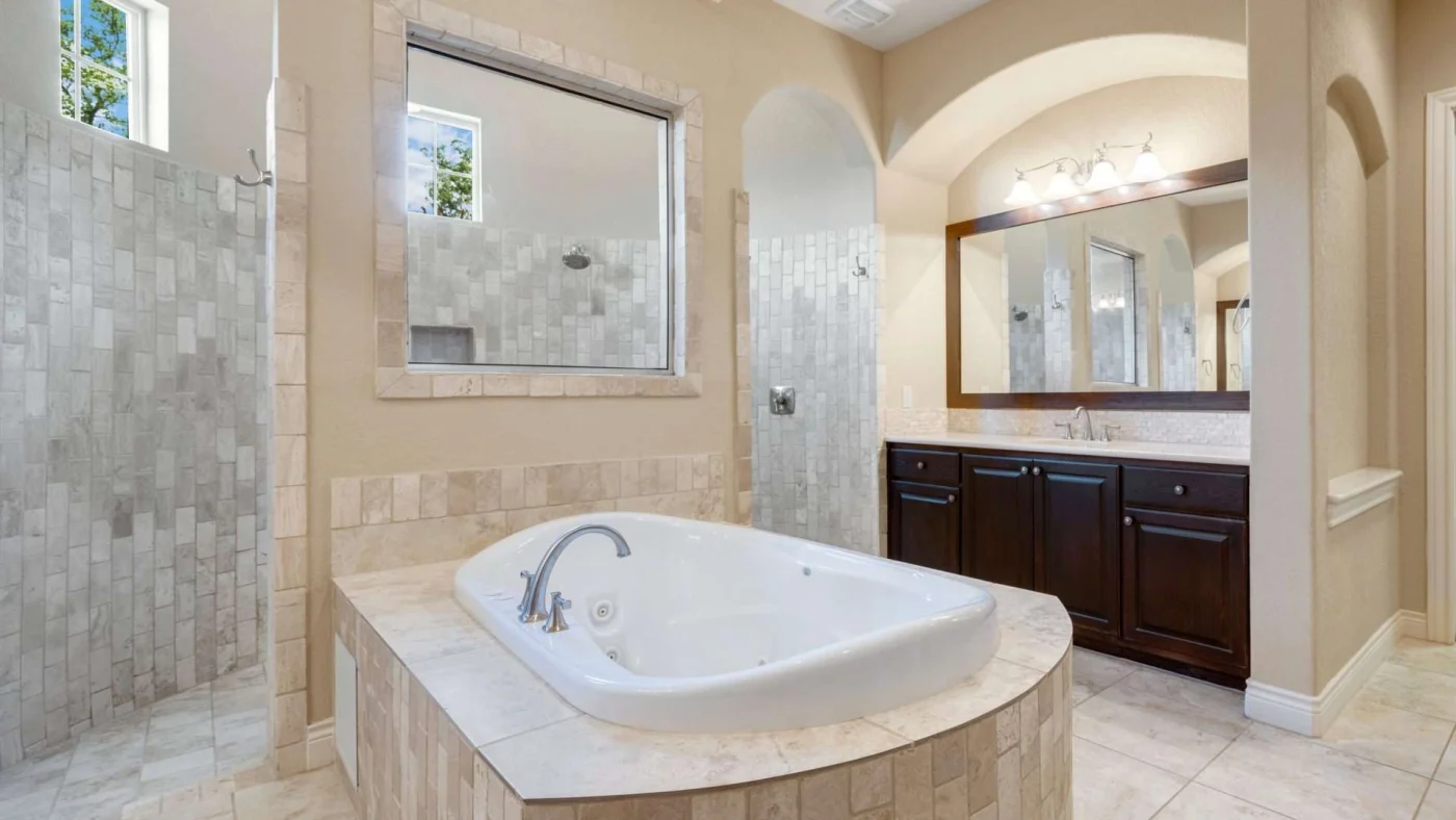 Angled view of a huge remodeled bathroom with a tiled, freestanding tub and a separate shower room in the background
