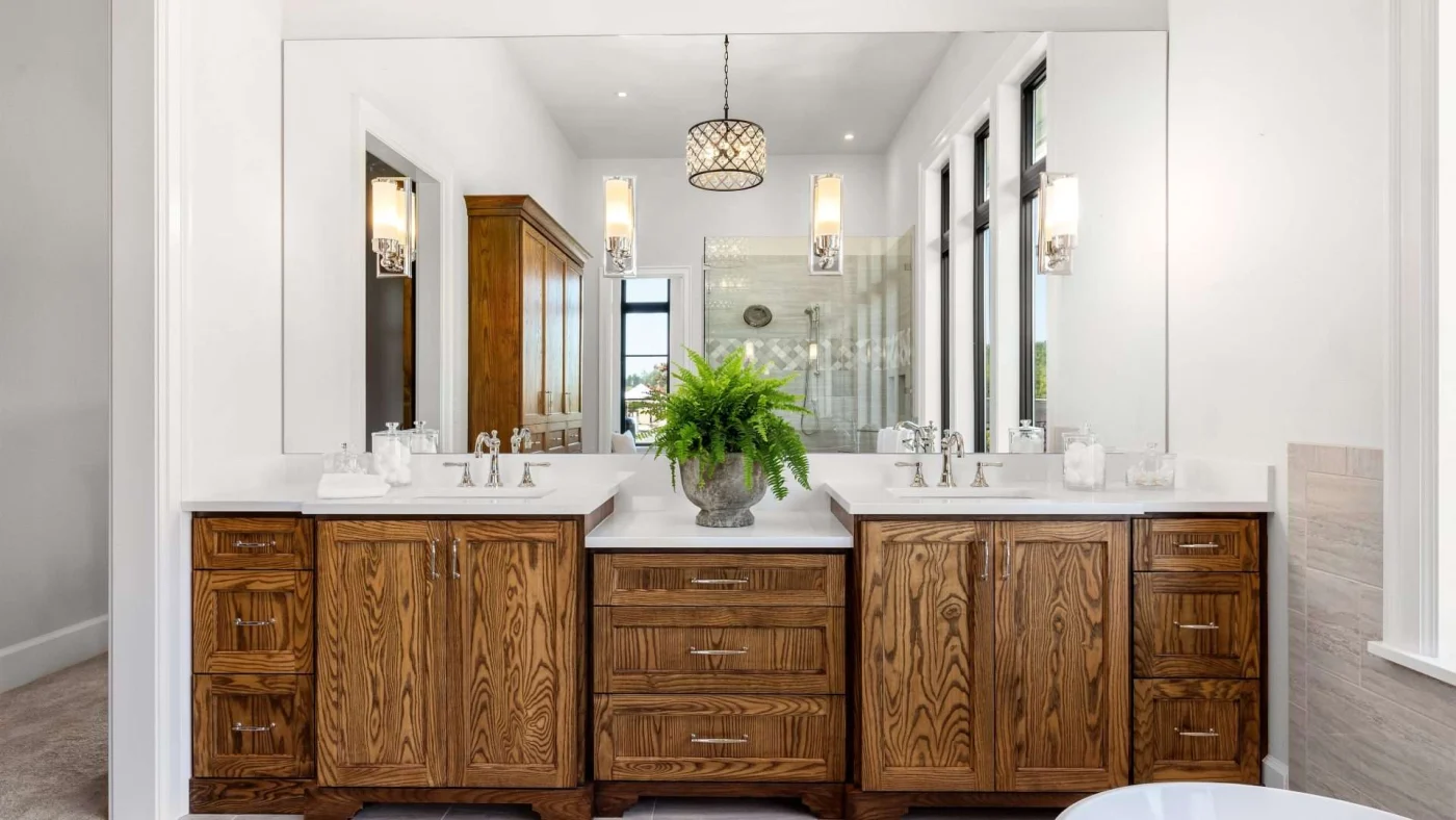 Frontal view of a large wood, double-sink vanity with a large mirror above it reflecting the rest of the bathroom