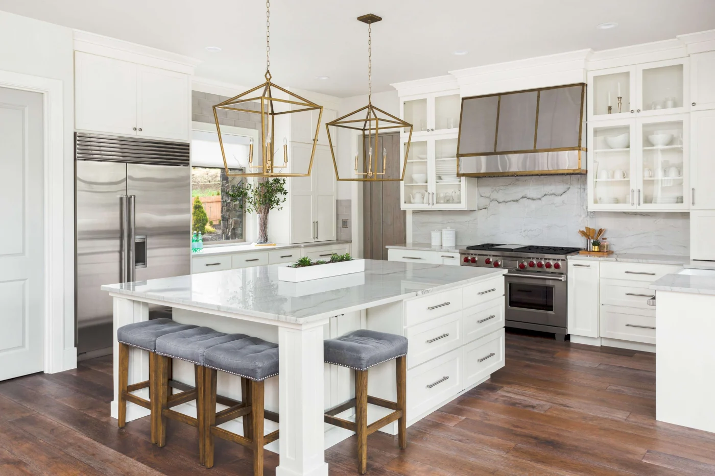 A modern, open-plan kitchen with a large center Island, white cabinets, marble countertops, and stainless steel appliances.