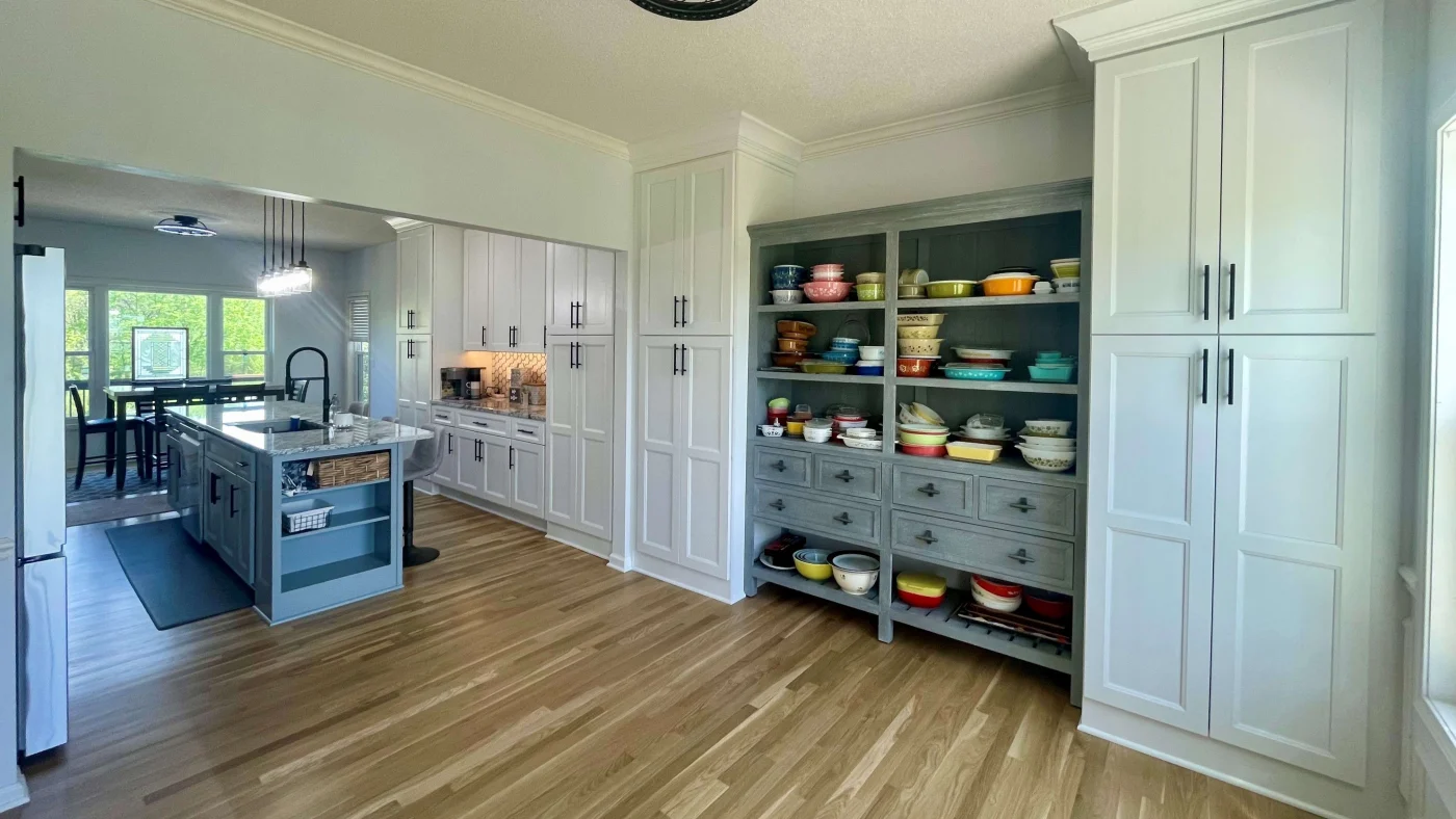 A spacious kitchen remodel with a large gray kitchen island, light countertop, tall white cabinets, and hardwood flooring.