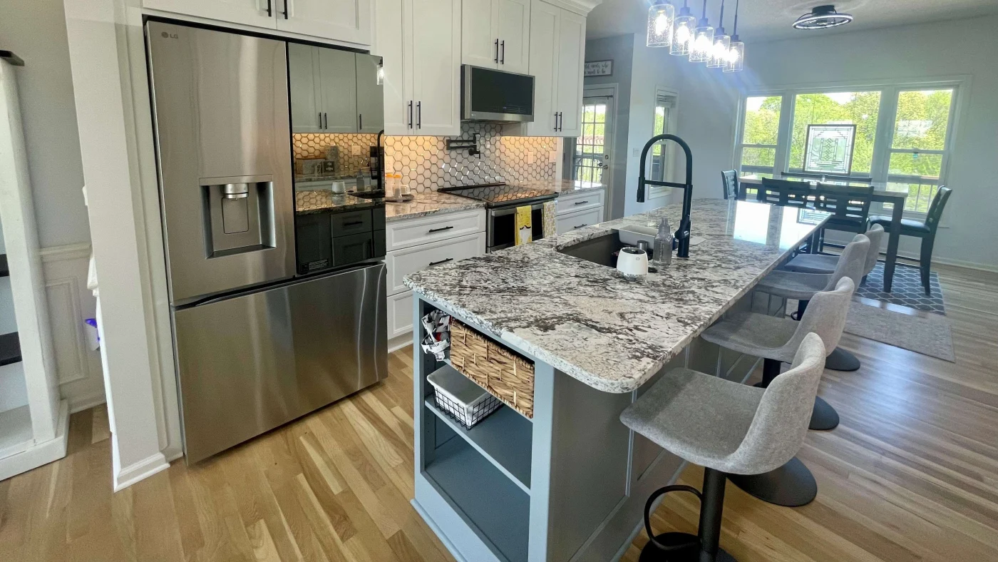 A modern kitchen remodel with white cabinetry, stainless steel refrigerator, granite countertops, a large center island with built-in shelving, and modern seating.