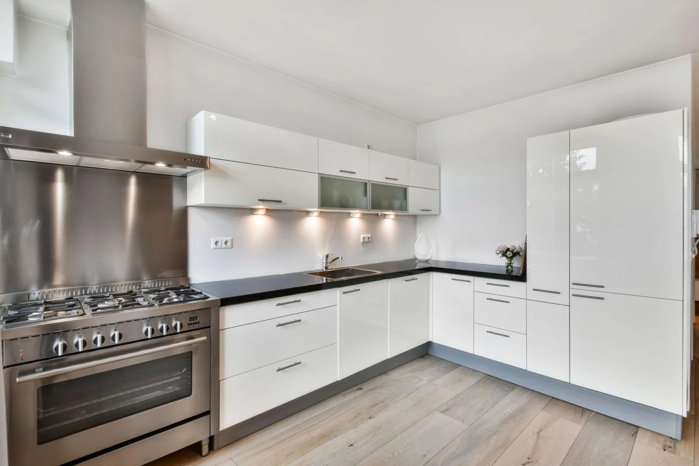 A newly updated kitchen with pale wood floors, white cabinets, stainless steel stove, and black granite countertops.