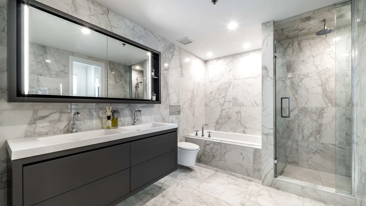 A modern bathroom remodel with a freestanding oval bathtub and a glass-enclosed shower with marble-patterned tile walls and floors.