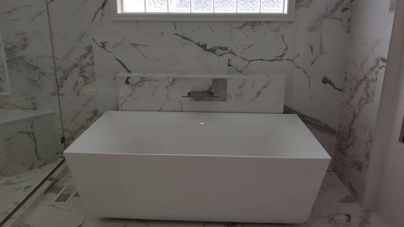 A modern bathroom remodel with a white freestanding rectangular bathtub, marble patterned backsplash walls and floor.