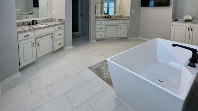 A modern bathroom remodel with a freestanding tub, Granite vanity tops, white cabinets, and spacious tile flooring
