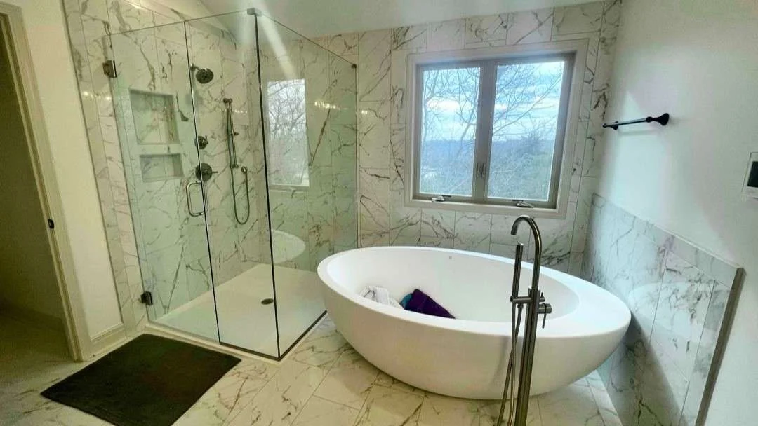 A gorgeous modern bathroom remodel with a freestanding oval bathtub, glass and glass-enclosed shower, and marble-patterned tile walls and floor