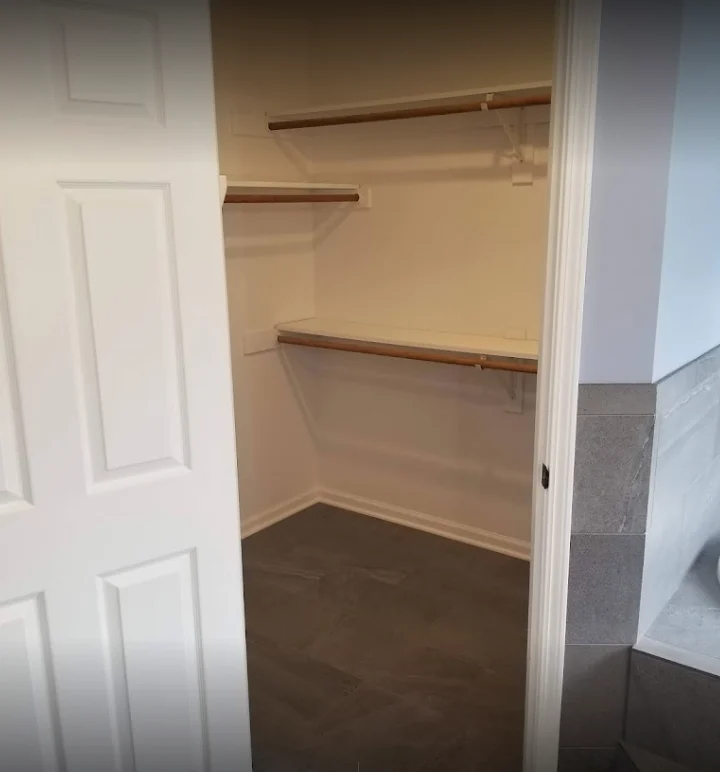 A new walk-in closet done as part of a master bathroom remodel by Jericho Home Improvements in a Kansas City home with new floating shelves with wooden hanging rods and white paint.