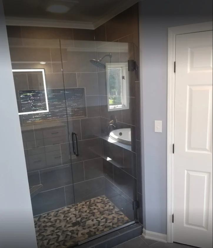 This is a brand new luxurious walk-in shower with custom tile flooring, new tile surround that matches the bathroom’s new tile floor, clear glass doors with a dark handle, and new larger showerhead.