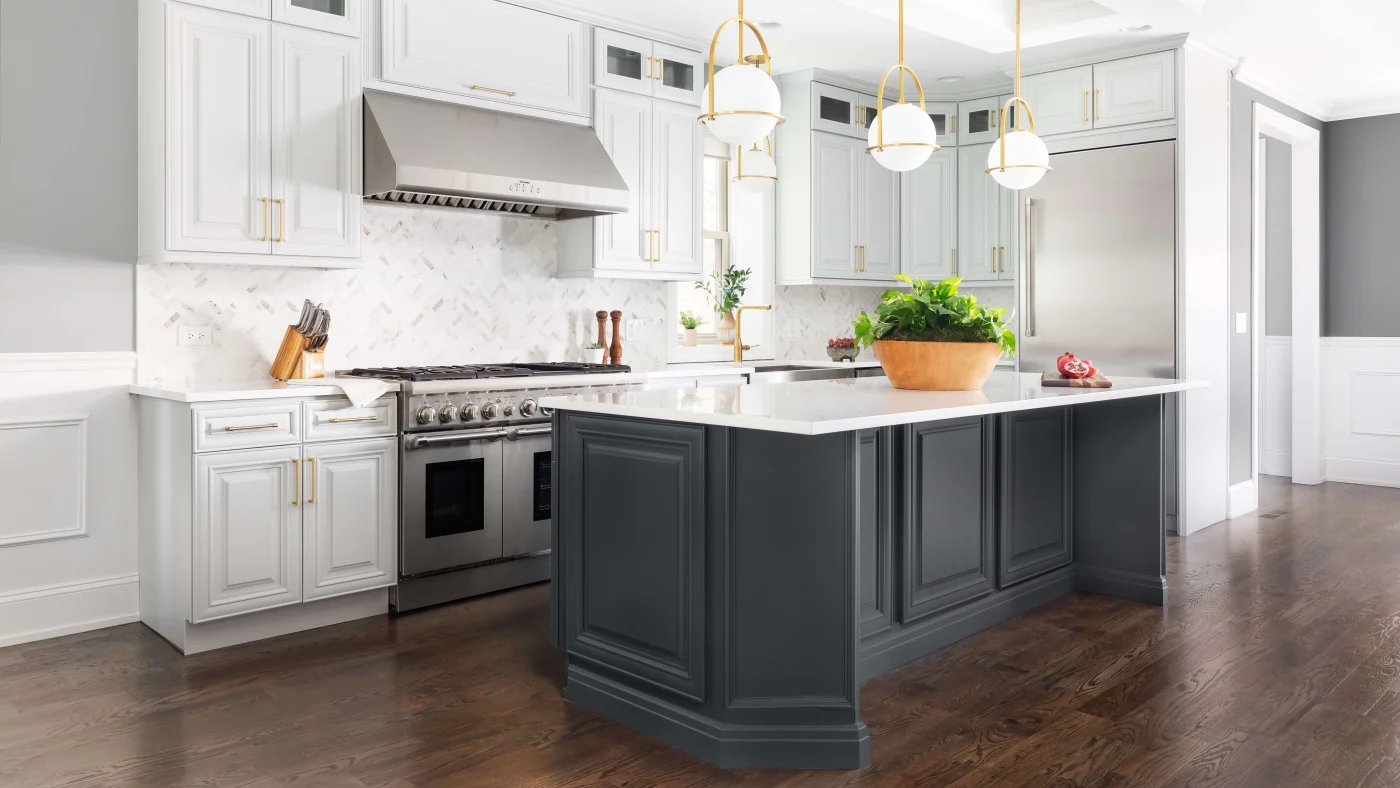 A modern kitchen remodel with white upper cabinets, a stainless steel range hood, and a dark gray kitchen island with white countertops and dark wood floors.