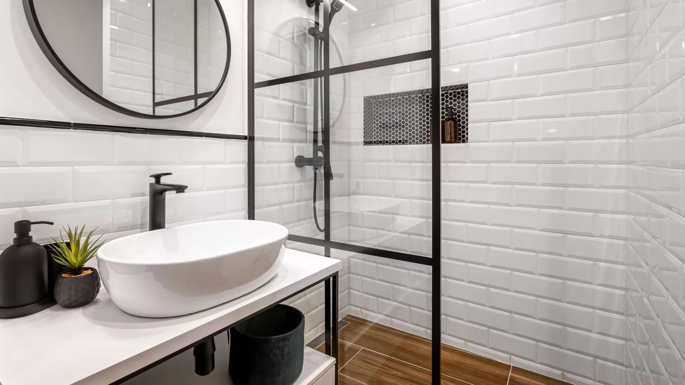 A gorgeous shower remodel with a half-glass enclosure, white tile walls, oval mirror, and a unique oval white bathroom sink