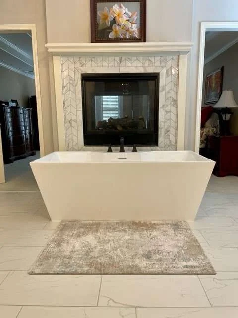 A modern master bathroom with a white rectangular freestanding bathtub in front of a fireplace with a black firebox.