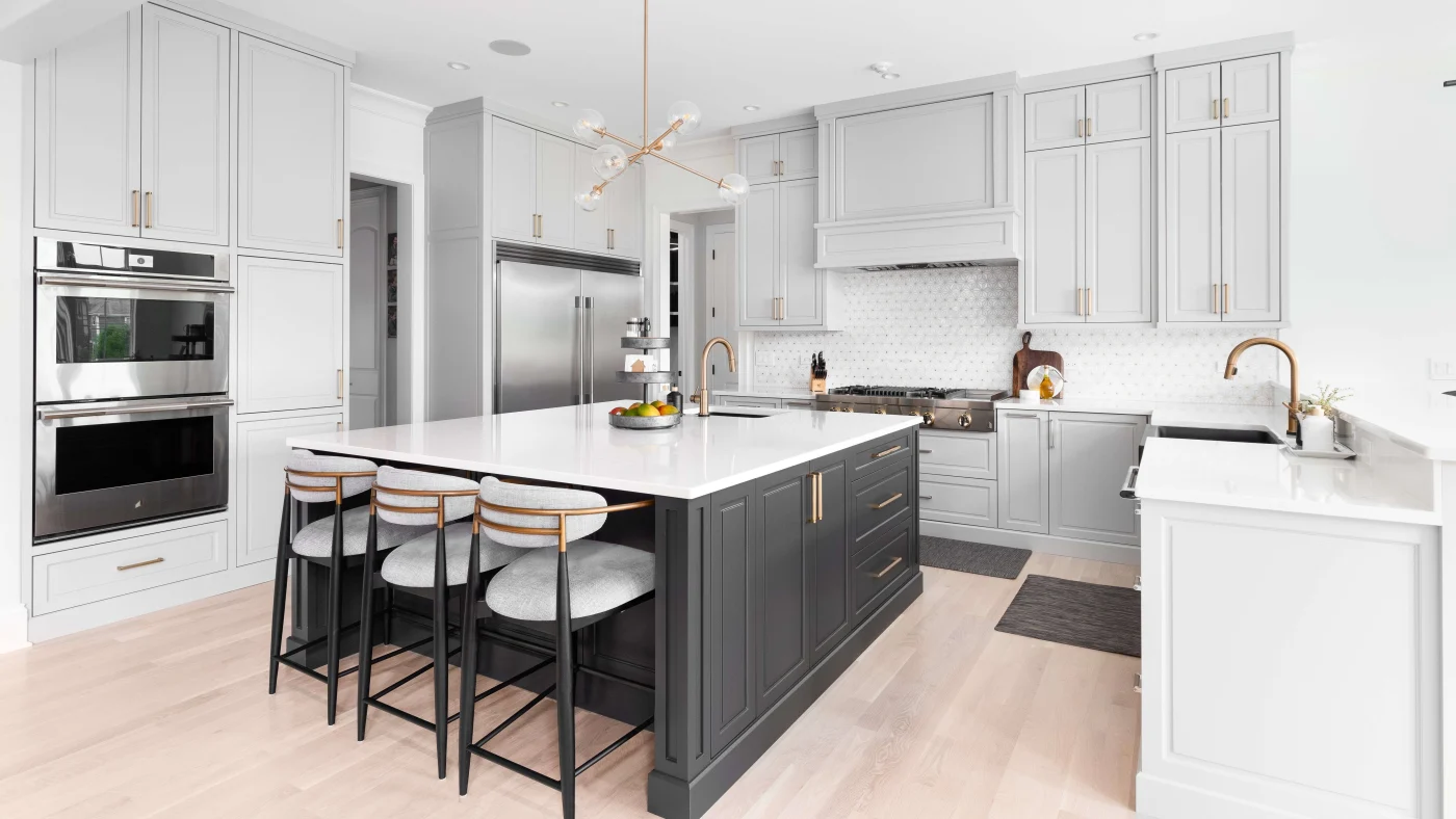 A modern kitchen remodel with a large island, light gray cabinets, stainless steel appliances, and white countertops.