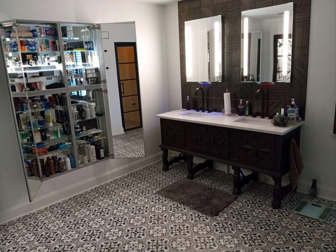 A modern bathroom remodel with a brown vanity with double sinks and mirrors, a mirrored medicine cabinet and patterned flooring