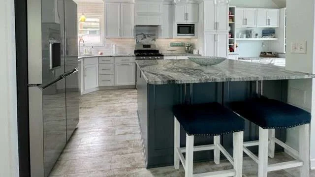 An elegant kitchen remodel featuring granite countertops, soft gray cabinets, stainless steel appliances, and a spacious center island with bar seating.